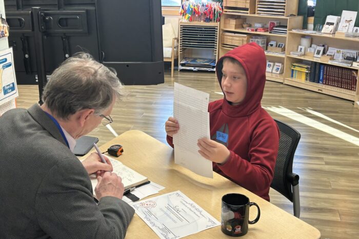 A student sits in front of a desk where a banker fills out a mock loan application