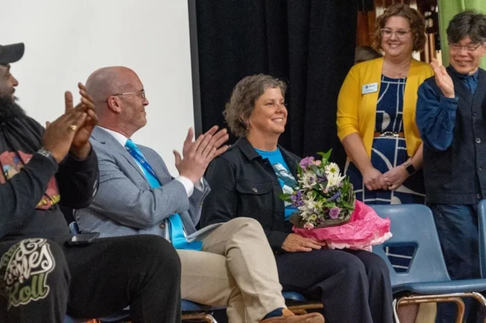 A seated woman, public Montessori school principal Katie Loss, is surrounded by clapping figures